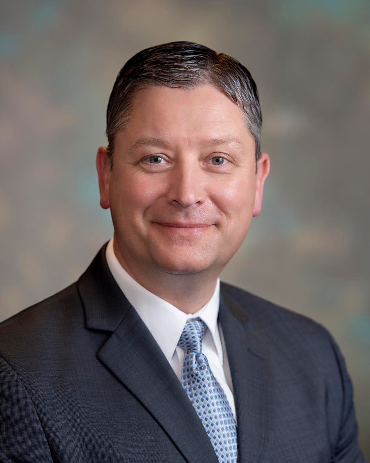 Portrait of a person in a formal suit with a neutral background