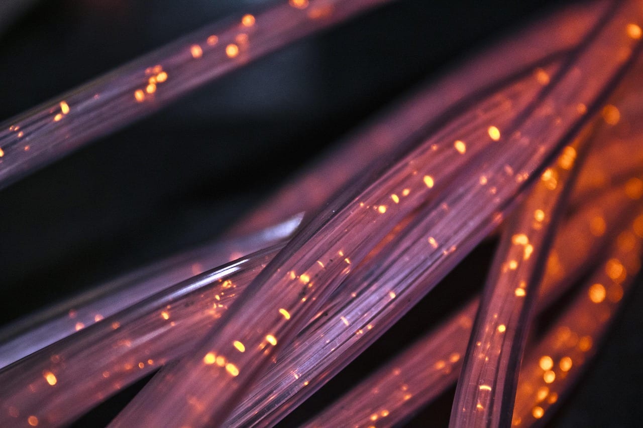 Macro shot of red and purple fiber optic cables glowing with orange lights, representing high-speed internet connectivity