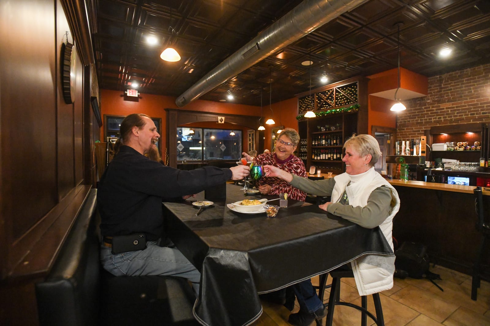 Three people sharing a toast at a table in Brown Street 151, a restaurant in downtown Rhinelander with a warm, rustic interior.