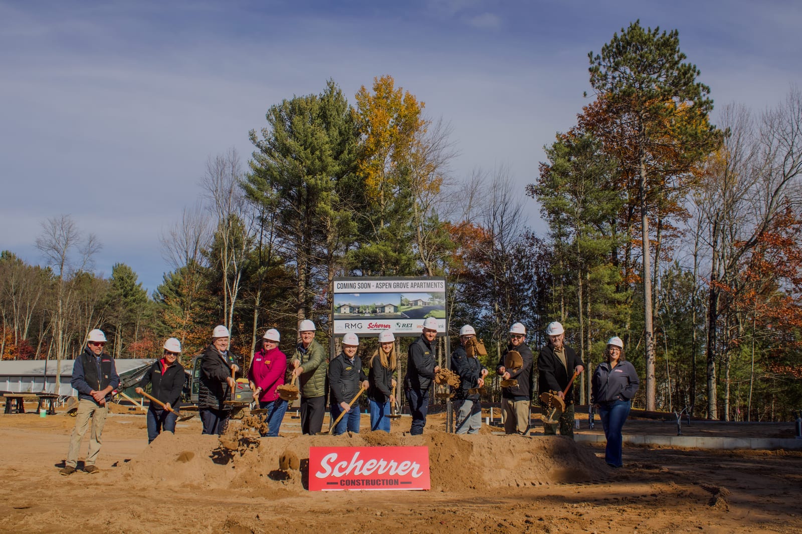 A group of people wearing hard hats participate in a groundbreaking ceremony on a construction site surrounded by fall trees in Oneida County, Wisconsin